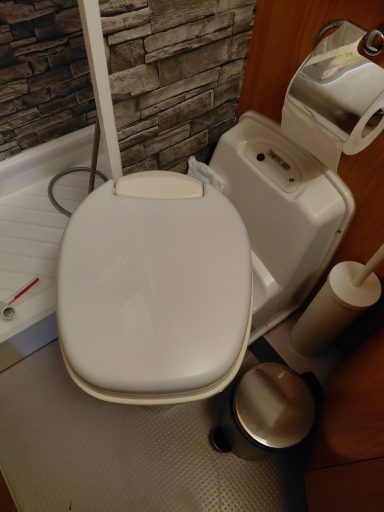 Toilettes blanches avec papier toilette et poubelle dans une salle de bain.